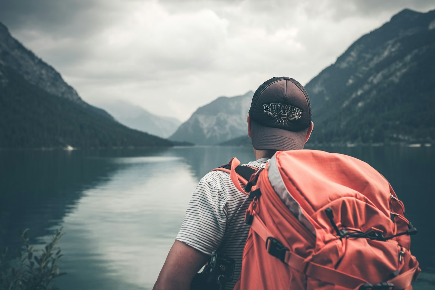 A traveler with a backpack looking out over a mountain lake