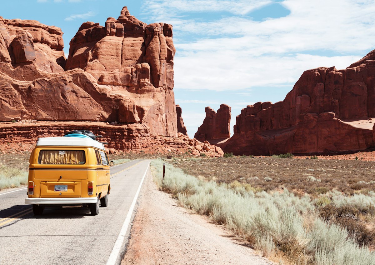 A camper van on a desert road between red rock formations