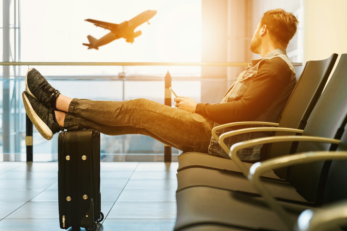 A traveler waiting at the gate as a plane takes off outside