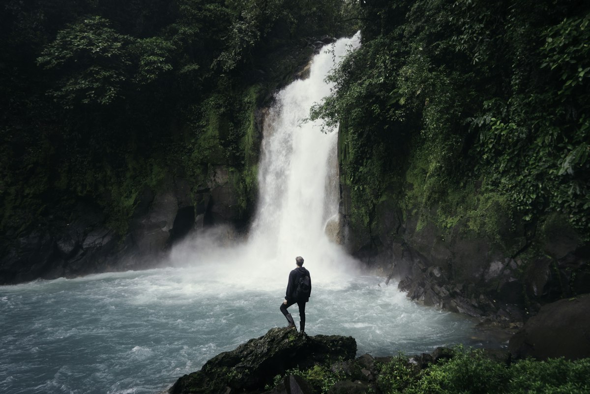 A traveler looking at a waterfall in a rainforest