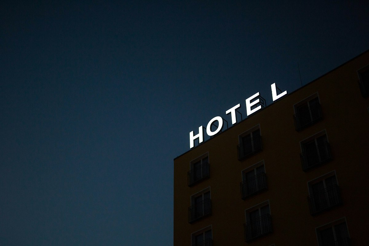 A neon hotel sign glowing on the corner of a building at dusk